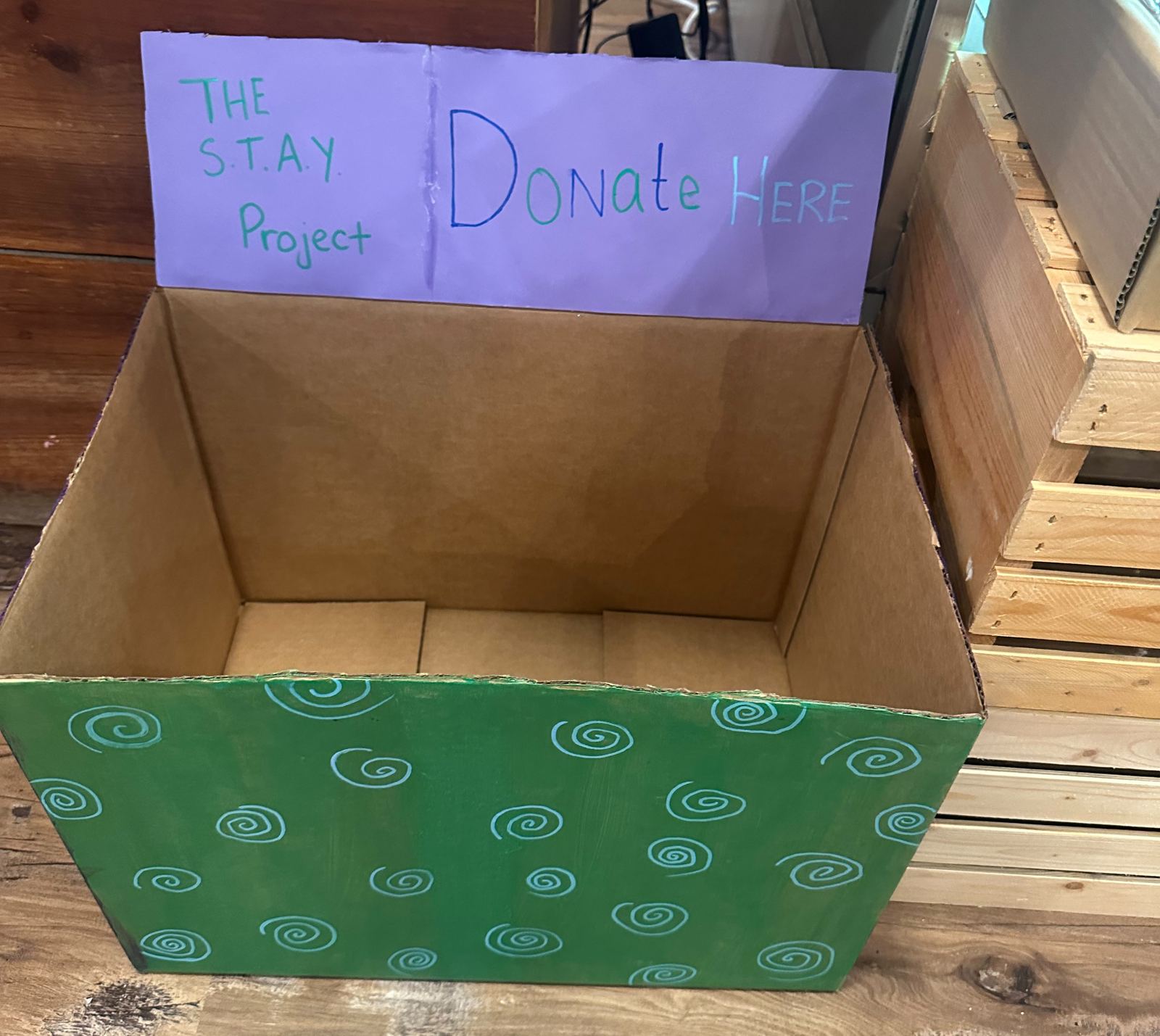 A STAY Project goods drive collection box with a handwritten Donate Here sign
